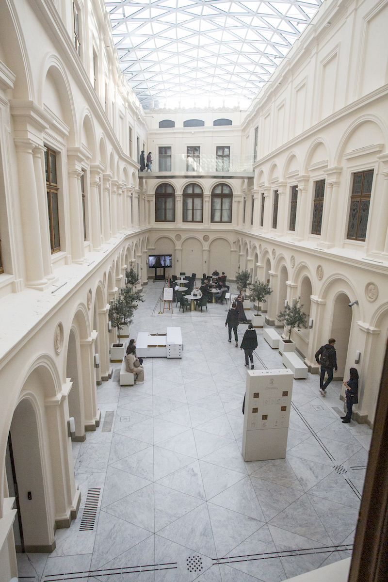 Zadaszony jasny dziedziniec. Wokół dziedzińca arkady. Po dziedzińcu kręcą się zwiedzający. Na jasnej podłodze ścieżki dotykowe.