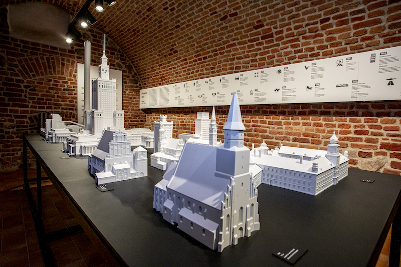 Na stole ustawione wydruki 3D najważniejszych budynków Warszawy. Wśród nich modele kościołów z wyraźnymi szczegółami elewacji.