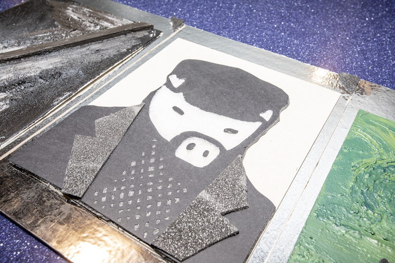 Tyflografika przedstawiająca postać z twarzą świni. Kształt postaci wycięty jest z kawałków czarnej gąbki o różnych fakturach. 