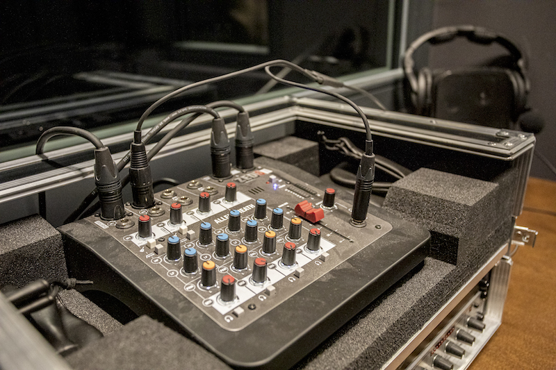 Wnętrze kabiny. Na stole konsola do regulowania dźwięku z wpiętymi kablami. Na panelu kilkanaście kolorowych przełączników i przycisków.