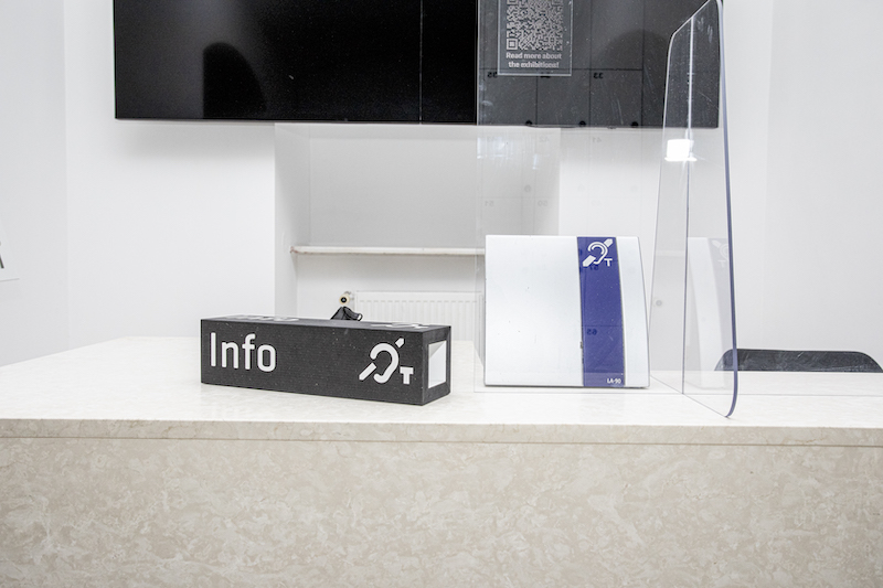 Lada punktu informacyjnego. Na ladzie tabliczka z napisem „Info” i symbolem pętli indukcyjnej. Obok druga tabliczka z granatowym piktogramem pętli indukcyjnej.
